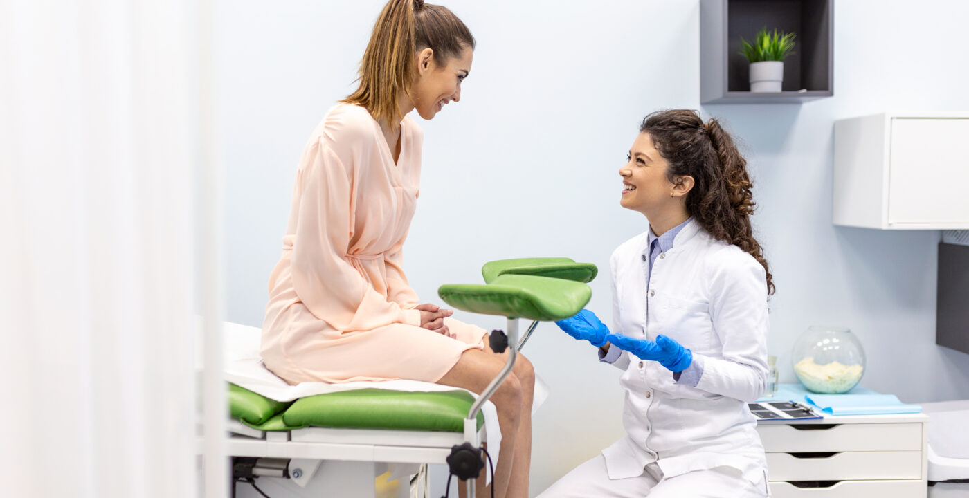 woman sits on clinic exam table talking with doctor