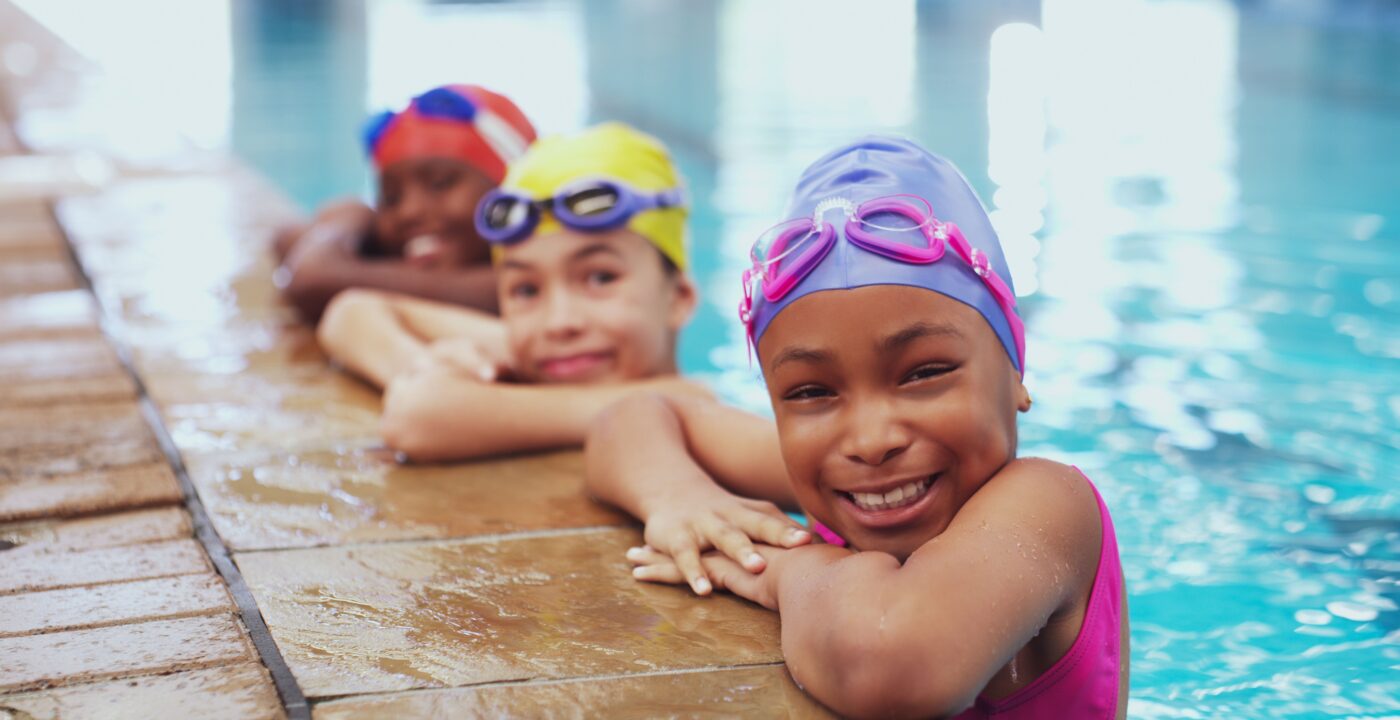 Three children holding on to the side of an indoor pool