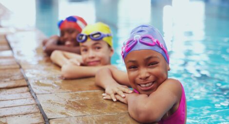 Three children holding on to the side of an indoor pool