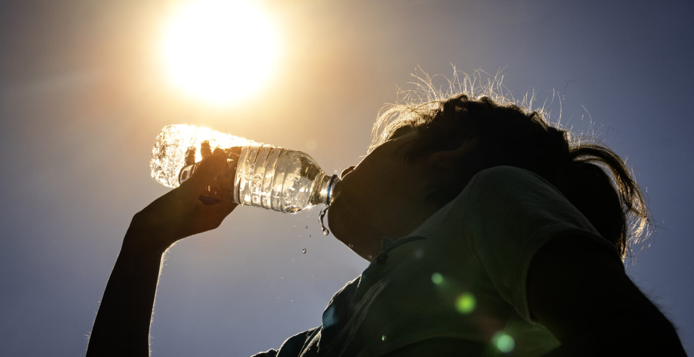 Young woman drinking fresh water from a plastic bottle under the hot summer sun