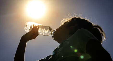 Young woman drinking fresh water from a plastic bottle under the hot summer sun