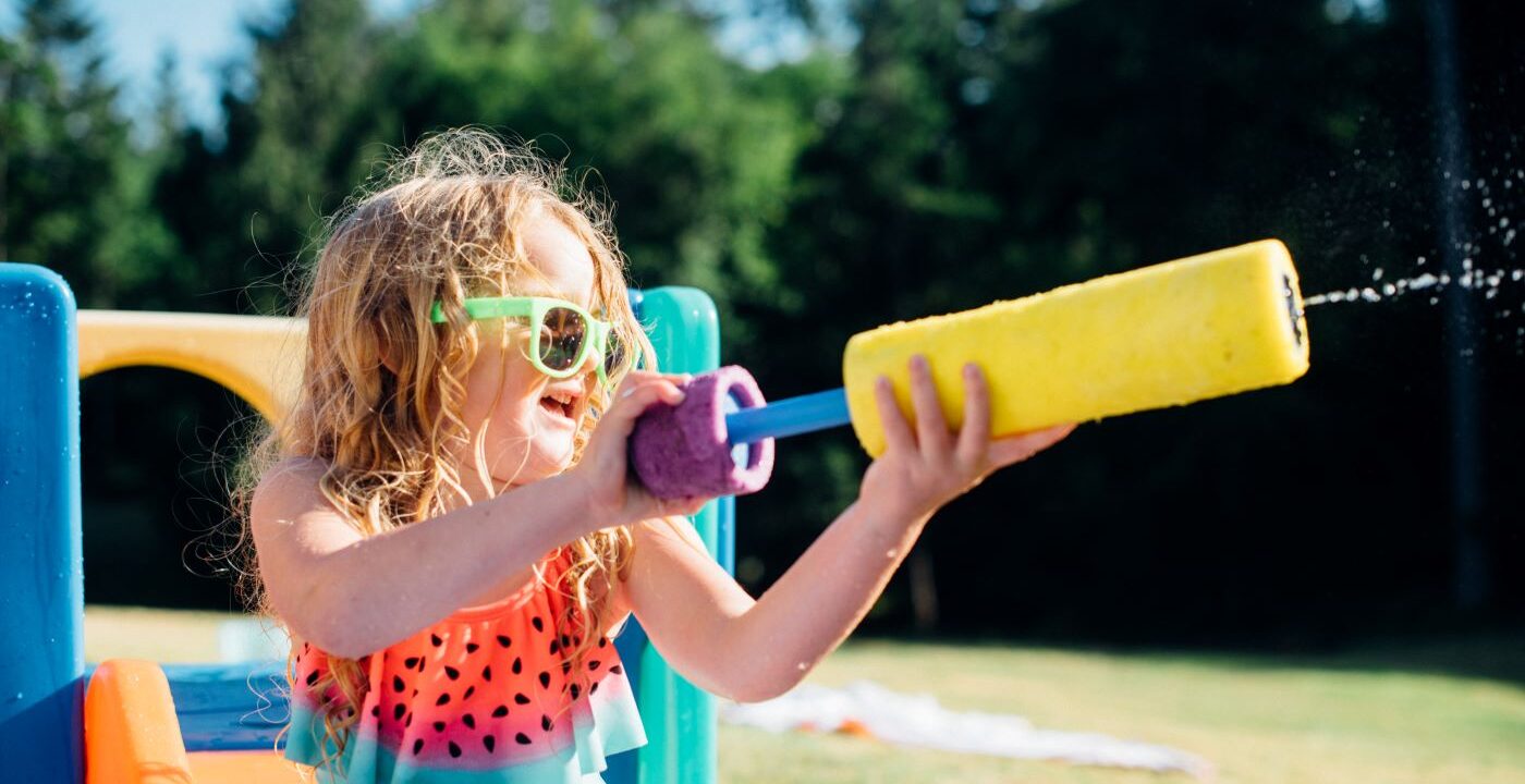 Little girl wearing sunglasses shoots a water gun on a sunny day.