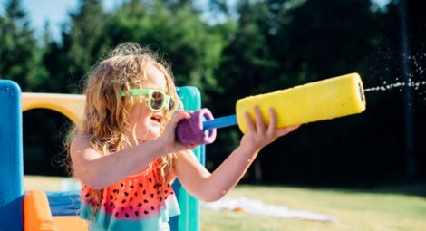 Little girl wearing sunglasses shoots a water gun on a sunny day.