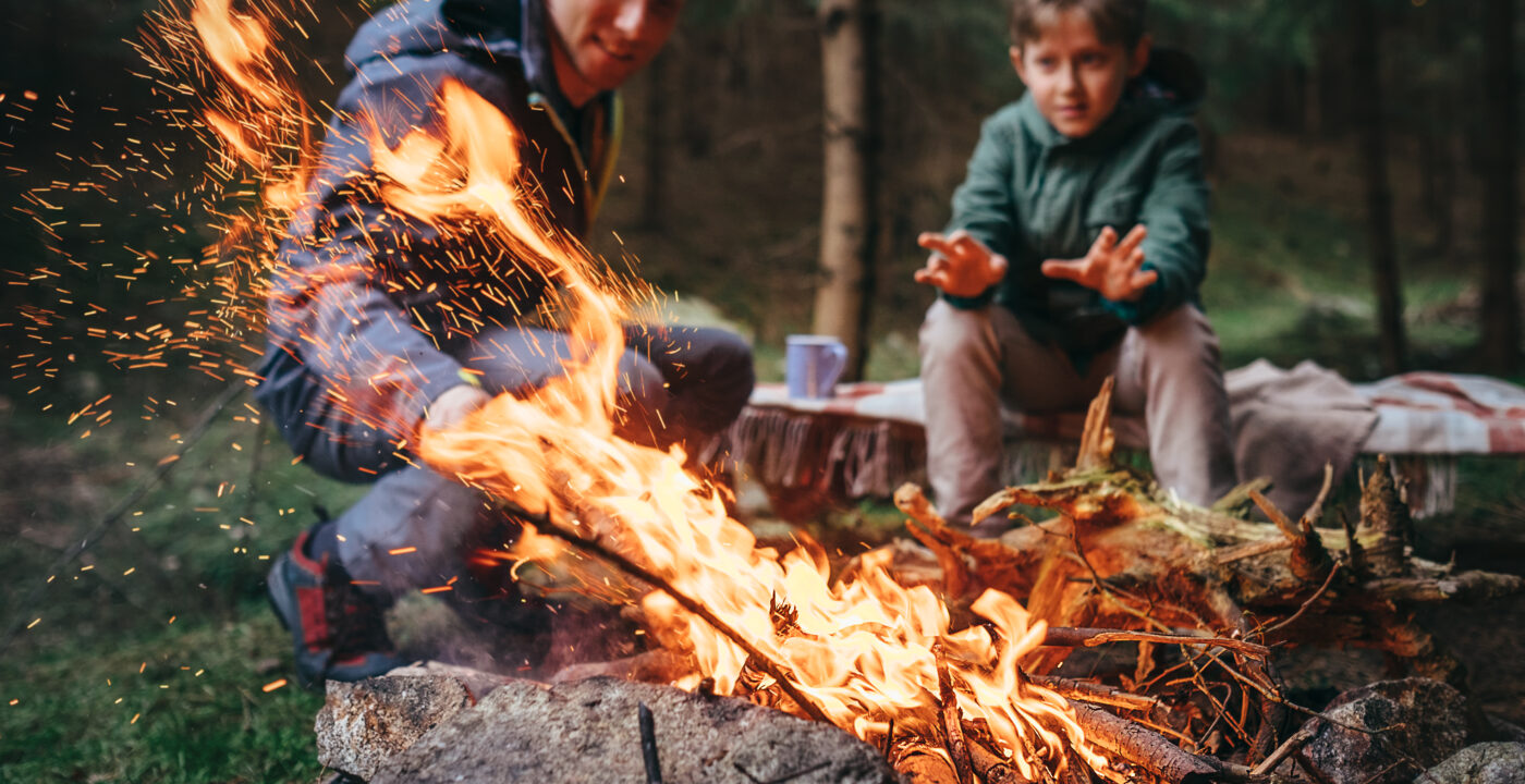 father and son sit behind campfire