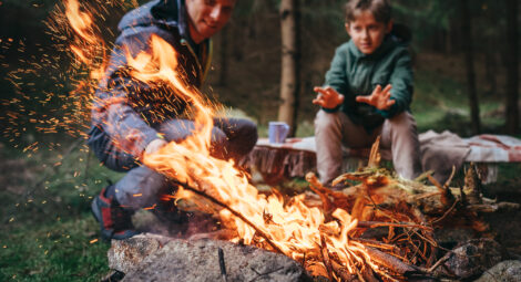 father and son sit behind campfire