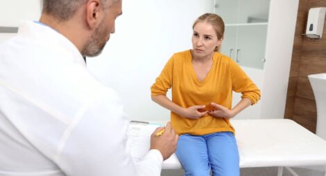 woman wearing orange shirt pressing on abdomen talking to doctor