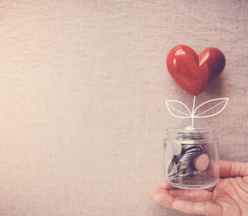 Hand holding a jar of heart tree growing on money coins, social responsibility and donation concept