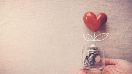 Hand holding a jar of heart tree growing on money coins, social responsibility and donation concept