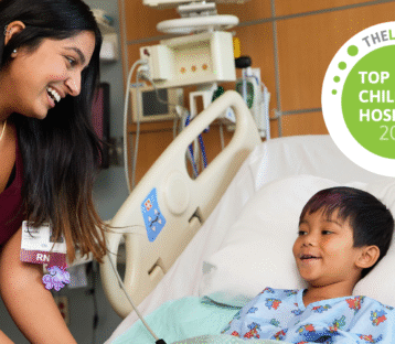 Nurse smiles at young boy in hospital bed