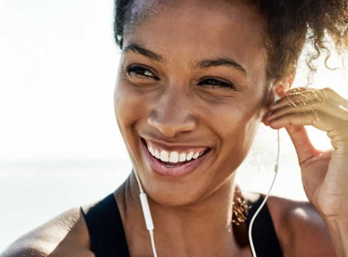 Woman smiles and puts headphone in her ear.