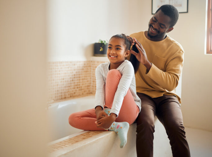 Dad and daughter smiling while dad does daughter's hair.