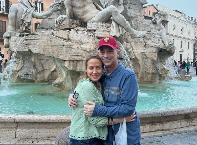 Tom & Donna Baker hug near a fountain in Italy