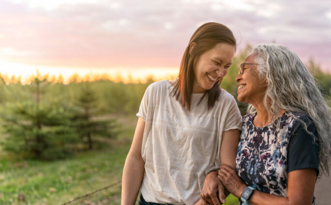 Two women walk arm in arm down a country road at sunset