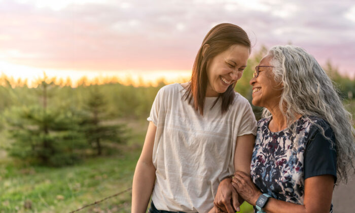 Two women walk arm in arm down a country road at sunset