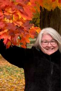 Dorena Roberts smiles next to a tree filled with autumn leaves