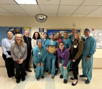 Colorectal surgery team poses for a group photo with their Center of Excellence plaque in a hospital hallway.