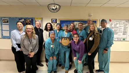 Colorectal surgery team poses for a group photo with their Center of Excellence plaque in a hospital hallway.