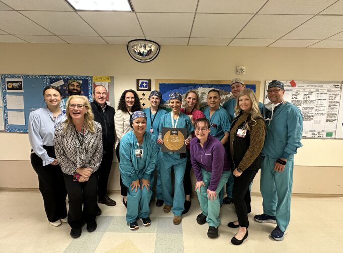 Colorectal surgery team poses for a group photo with their Center of Excellence plaque in a hospital hallway.
