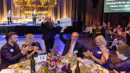 At a banquet table, Bill Robertson holds up a large envelope that reads Howard S. Wright.