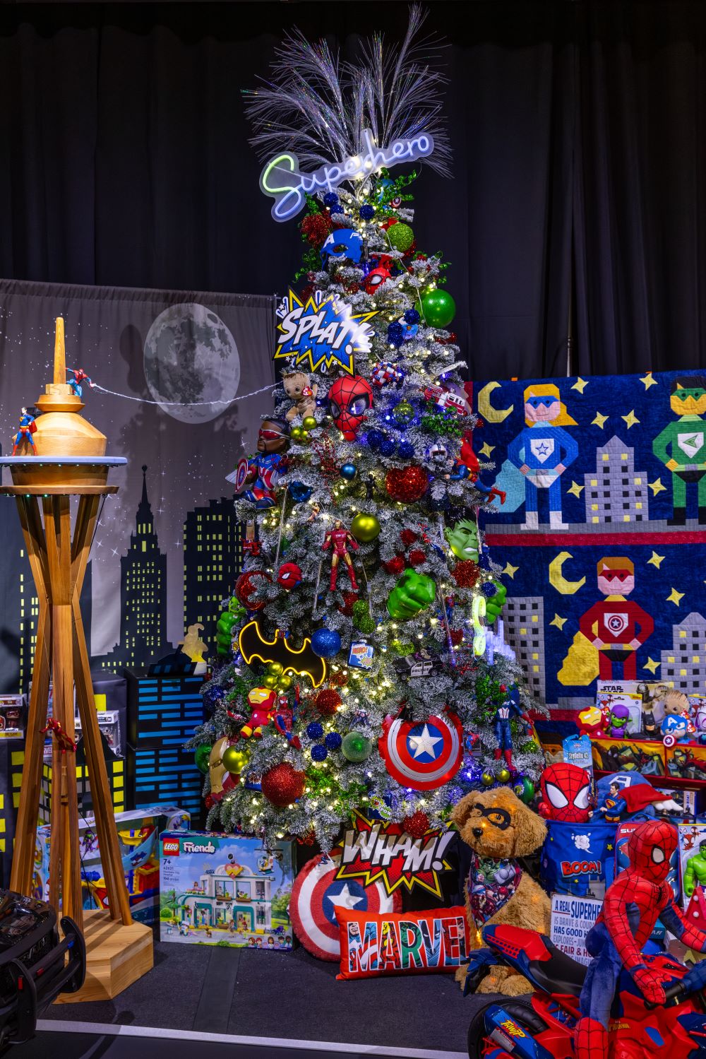 A superhero-themed tree gleams neon-bright against a handmade quilt and Space Needle, and unites the Marvel Avengers, Captain America and Spiderman among other masked doers of justice.
