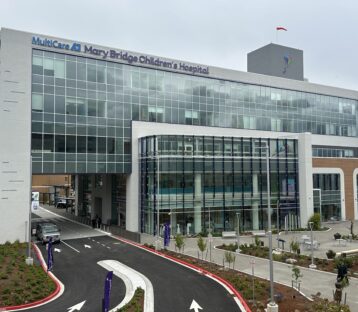 Exterior view of MultiCare Mary Bridge Children’s Hospital, showing a modern glass‑fronted building with the hospital name displayed above the main entrance and a curved driveway in front.