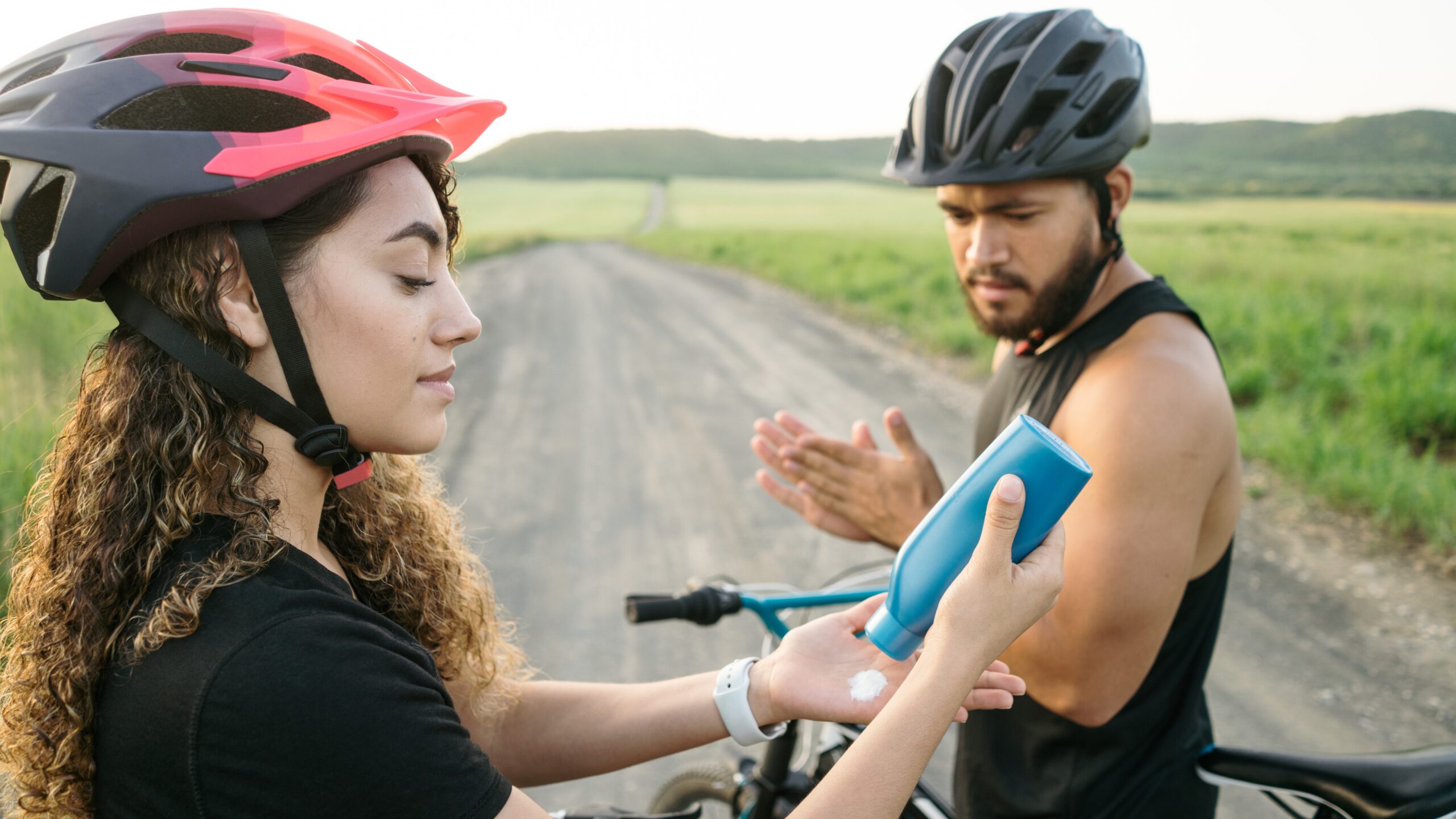 Two people on bicycles breaking to apply sunscreen.
