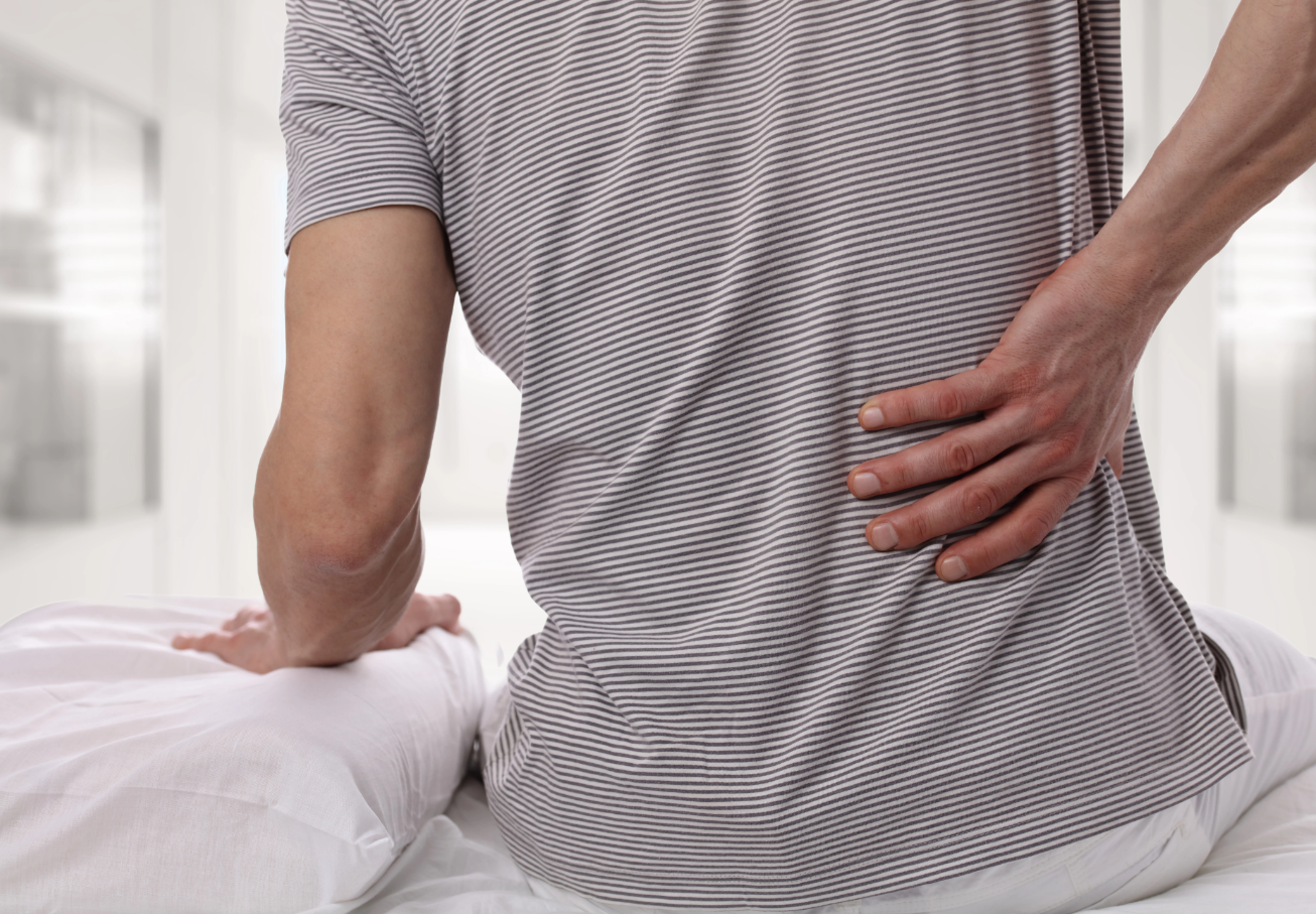 Person sitting on a bed and holding their low back in pain
