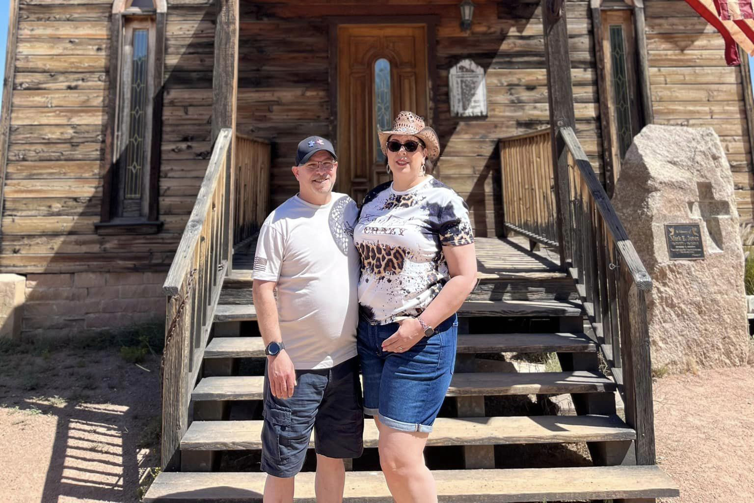Couple stands in front of a rustic building.