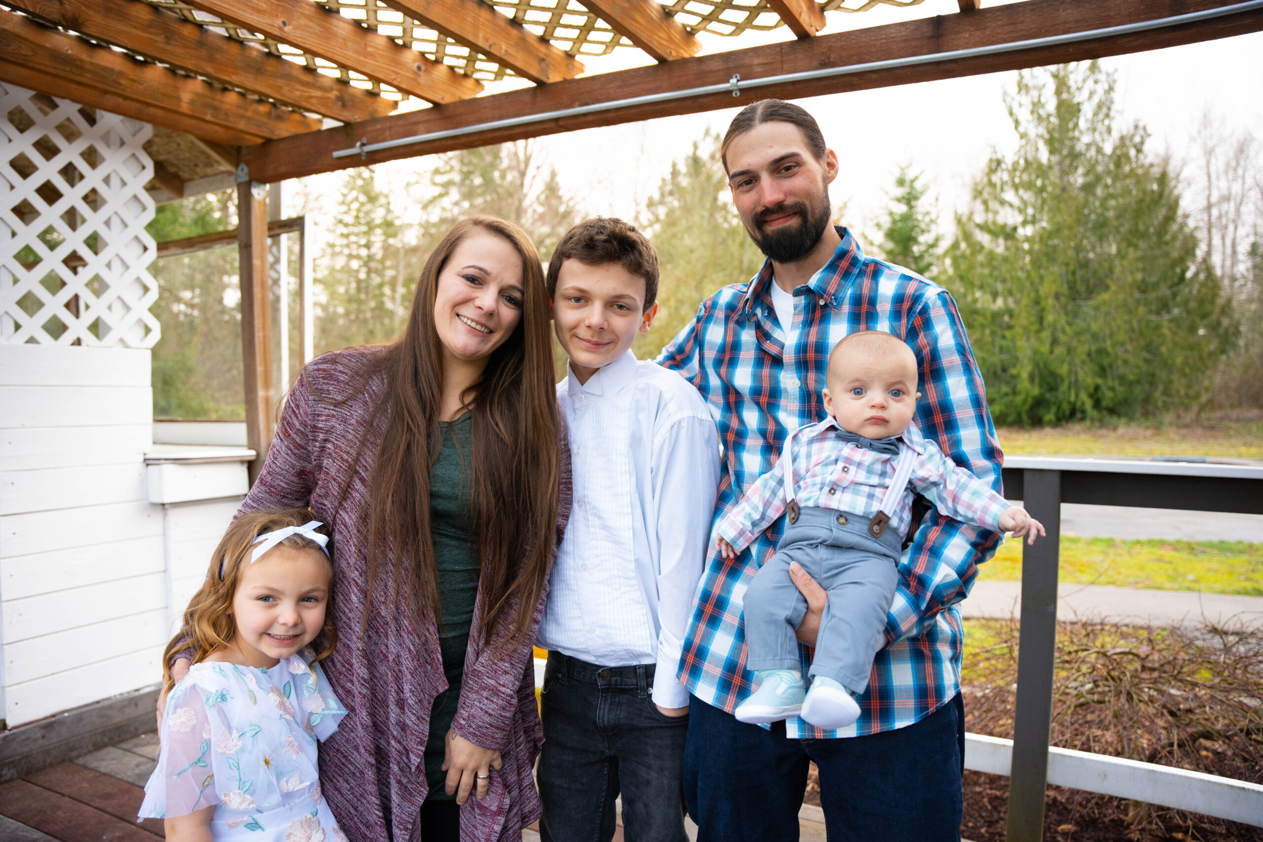 Mom, dad and three children pose on a deck outdoors