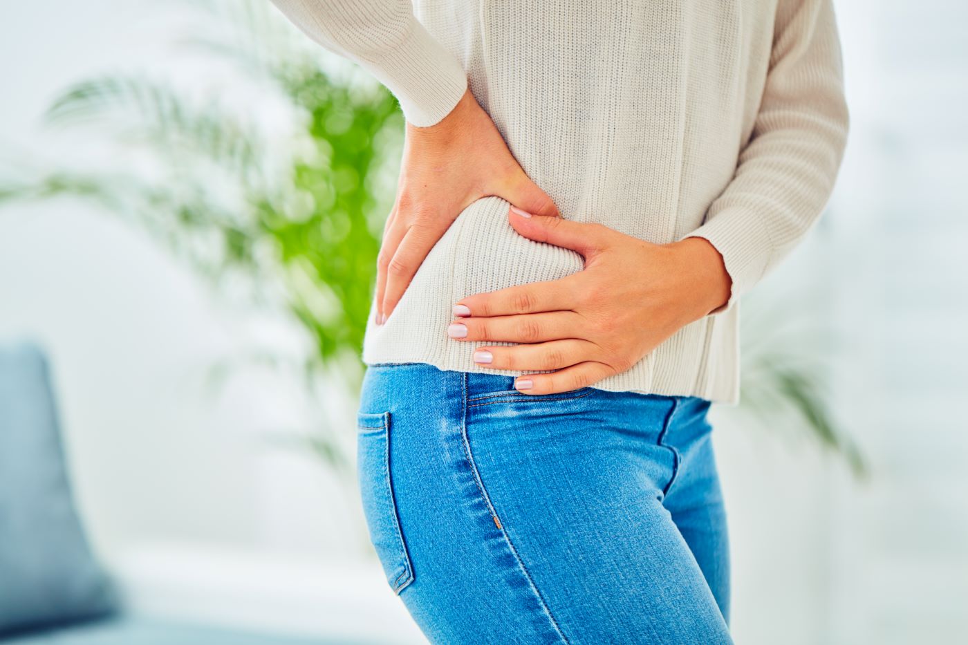 Torso of woman in sweater and jeans gripping right hip.