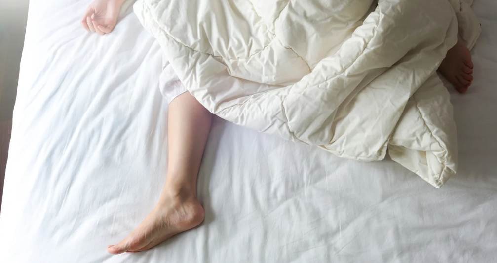 A young woman’s bare feet sticking out of a white comforter