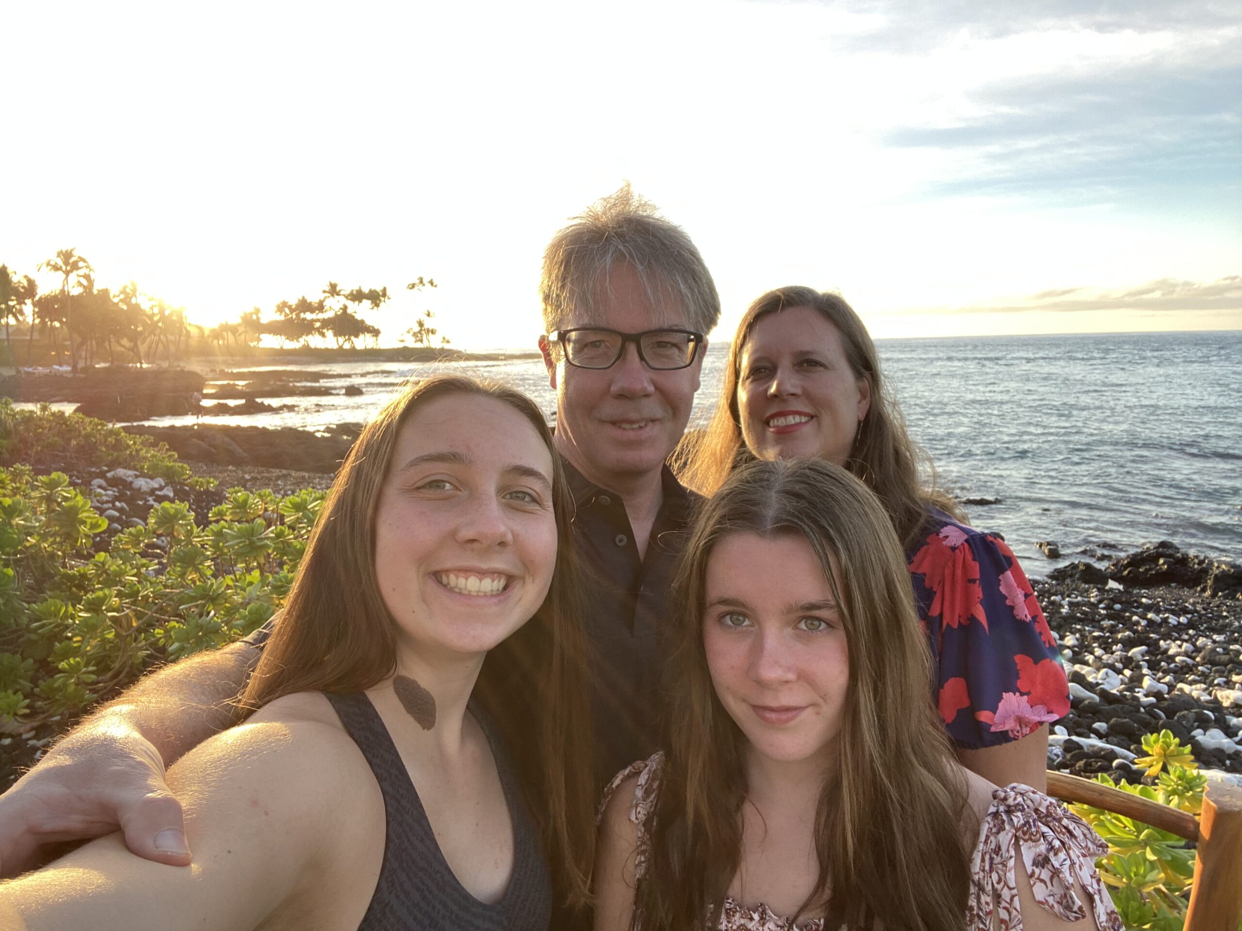 Dad, mom and two daughters smile for a selfie on the beach
