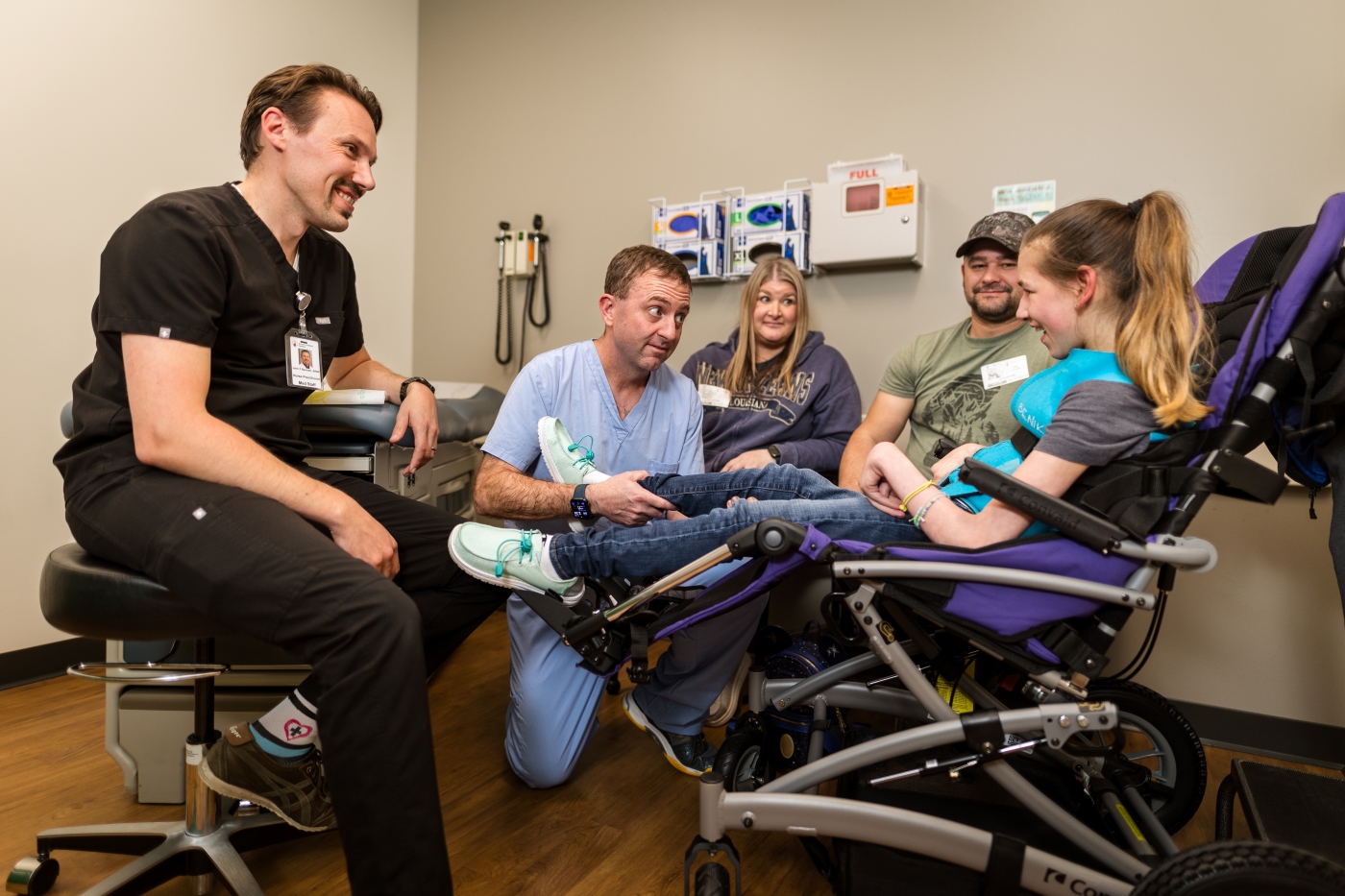 Two doctors speak with a patient in a power wheelchair while her parents sit nearby