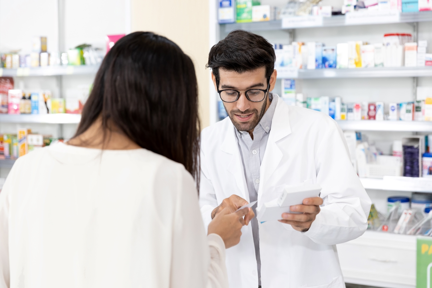 Male pharmacist reviews a prescription with an individual pictured from the back