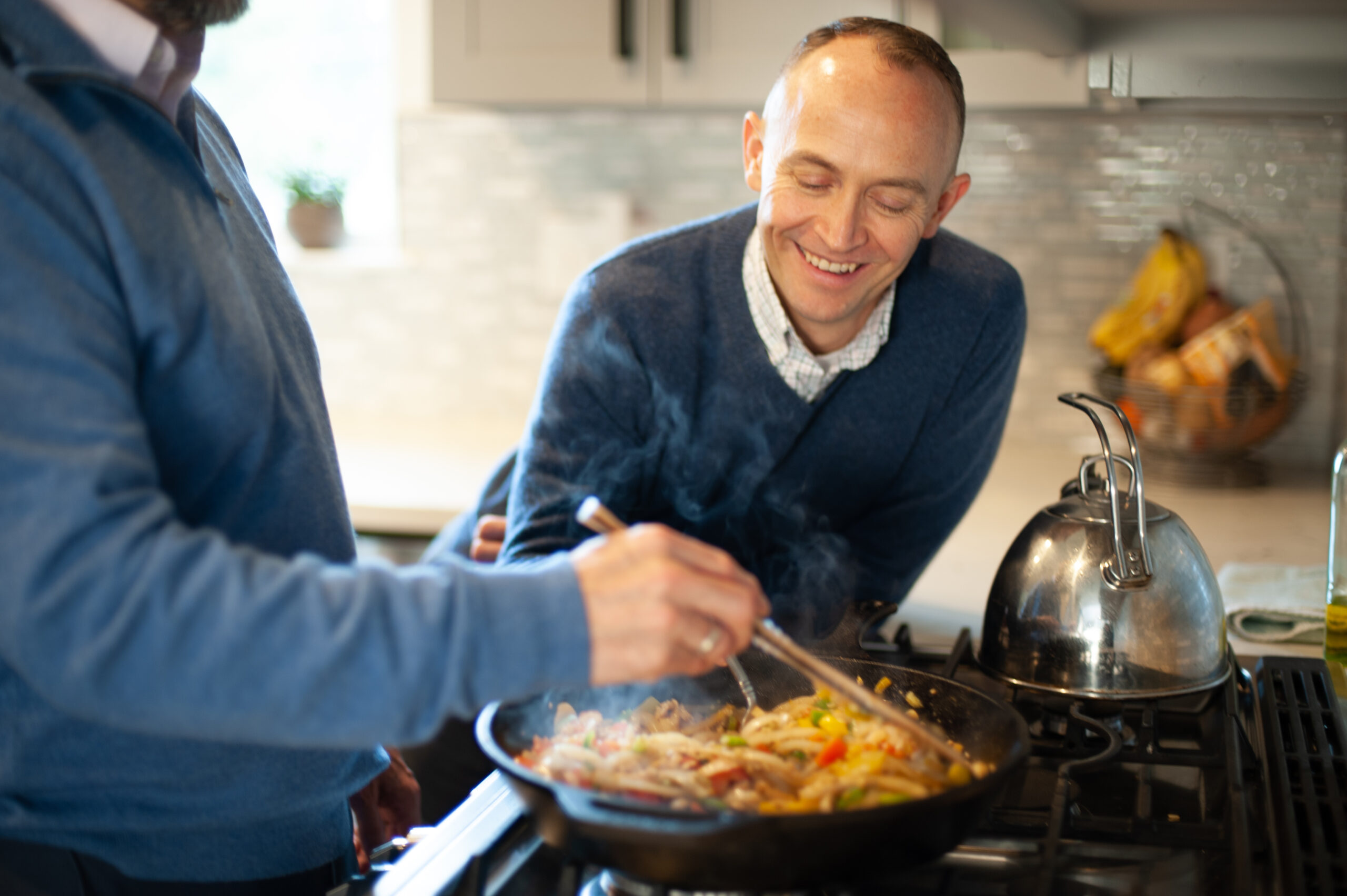 Two men stir a pan of food in a kitchen