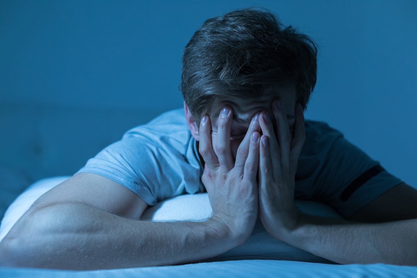 A man leaning on his pillow and covering his face with his hands