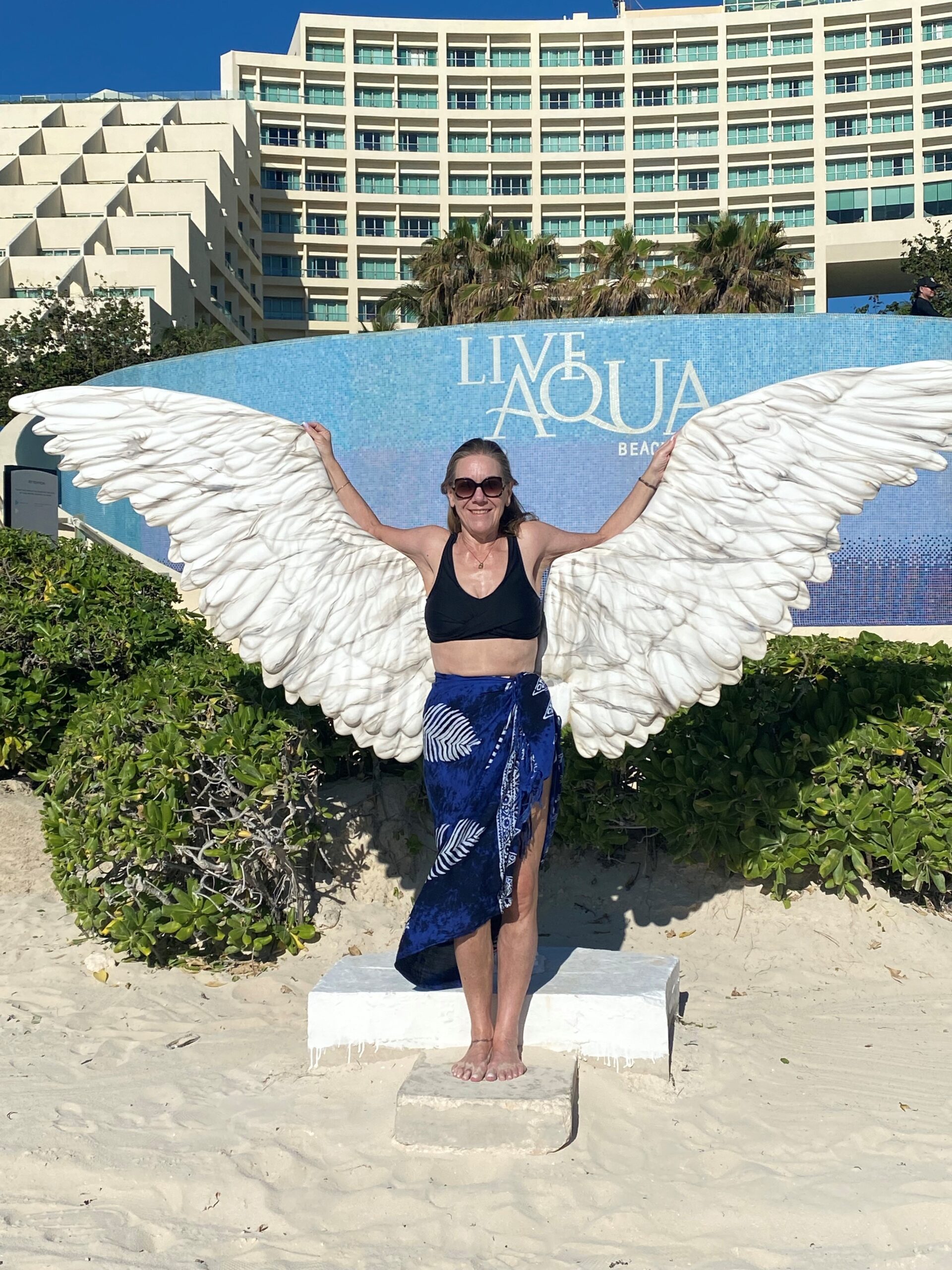 Woman on beach poses in front of statue of wings