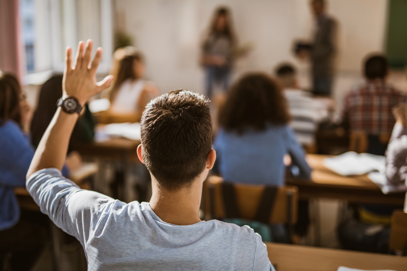 Student in classroom with their hand up, seen from the back