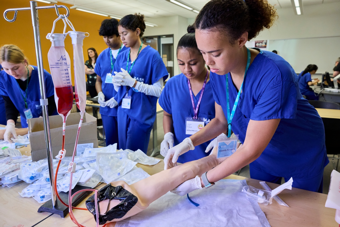 Students in scrubs examine fake arm