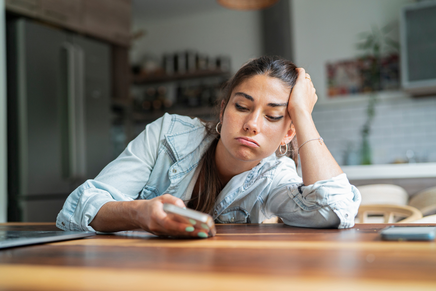 tired woman leans on table and looks at phone