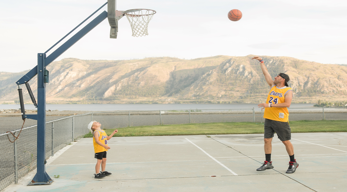 Man shooting basketball with child watching