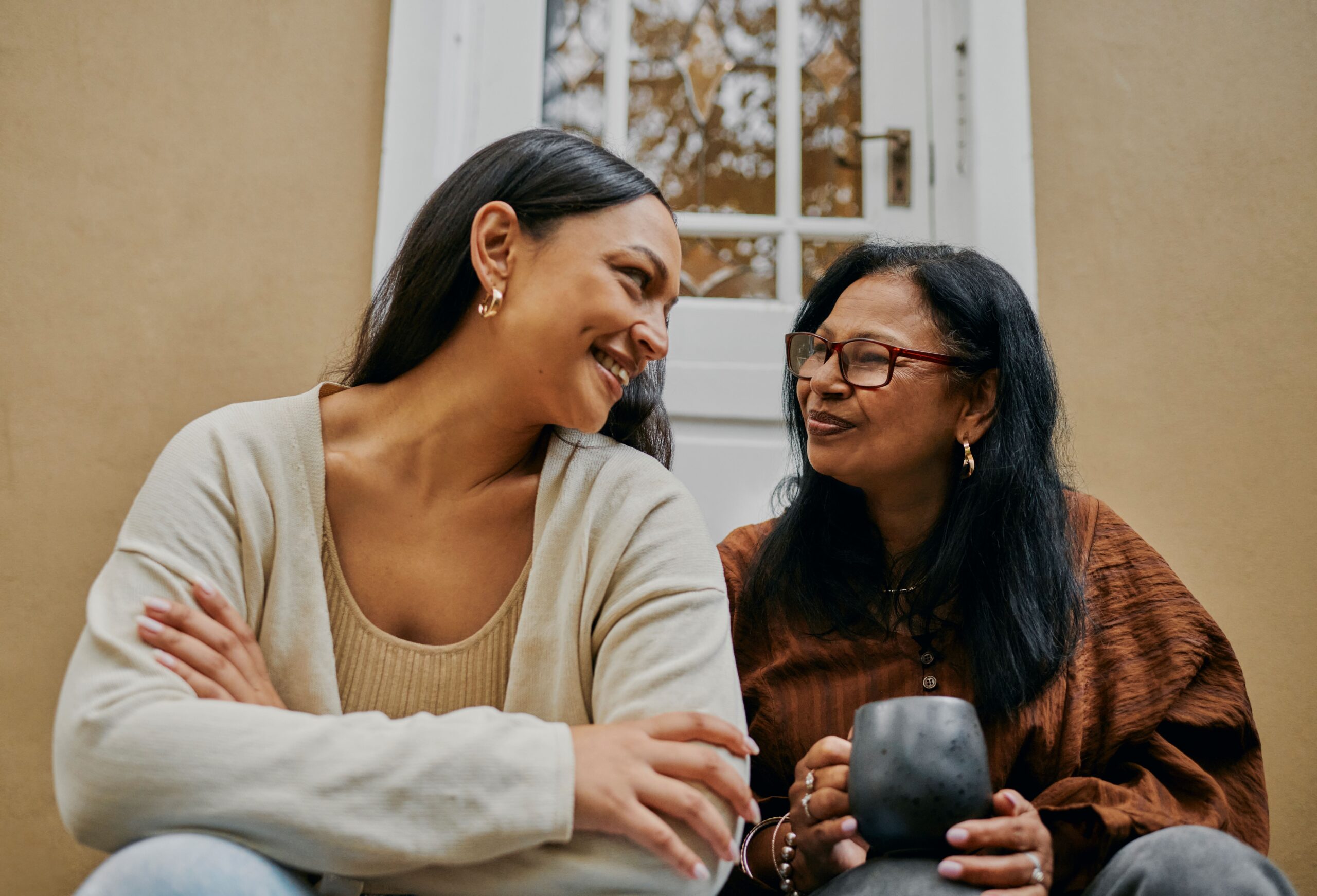 Mother and daughter sit together and smile on their front steps.