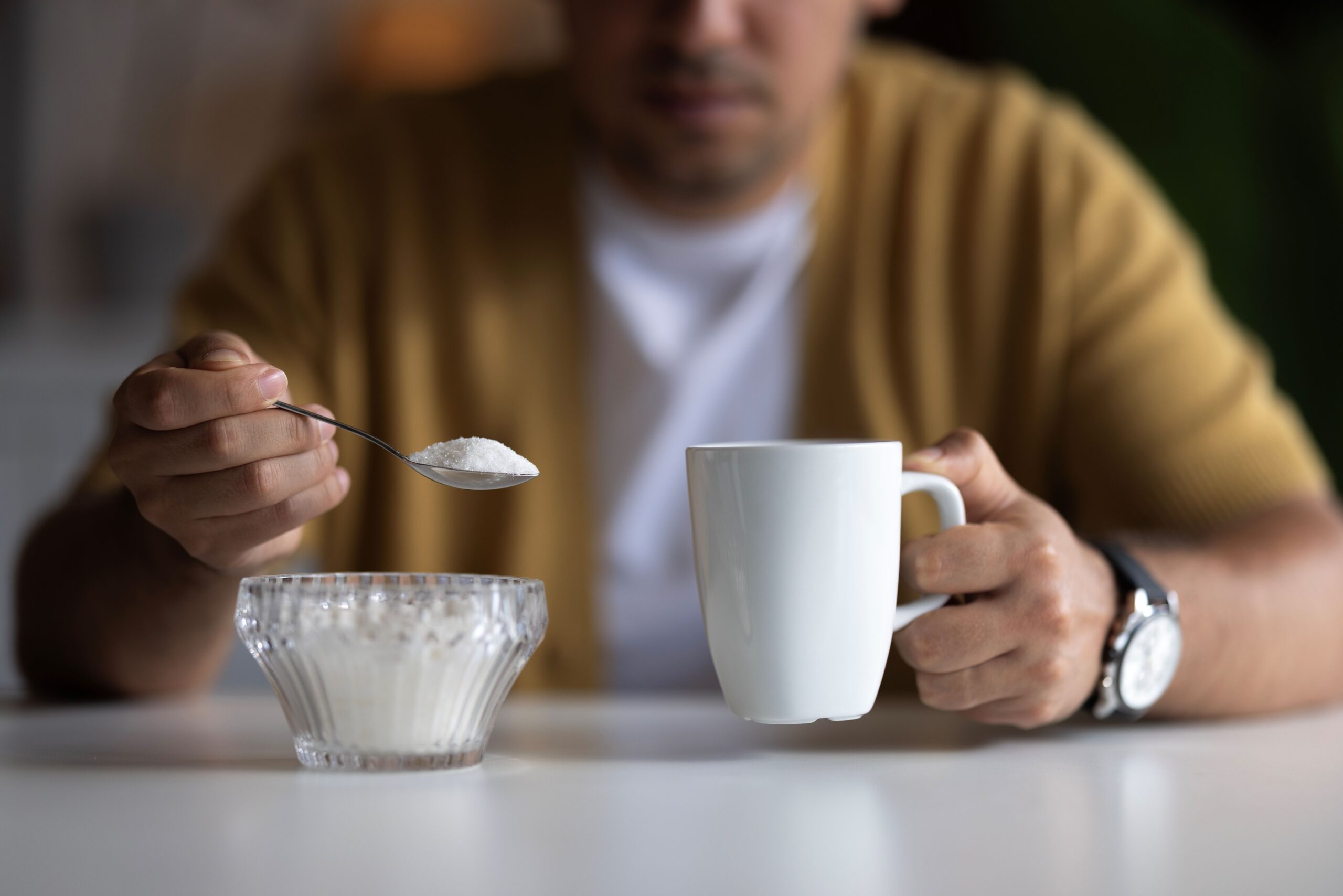 Man holding a spoonful of sugar and a coffee cup