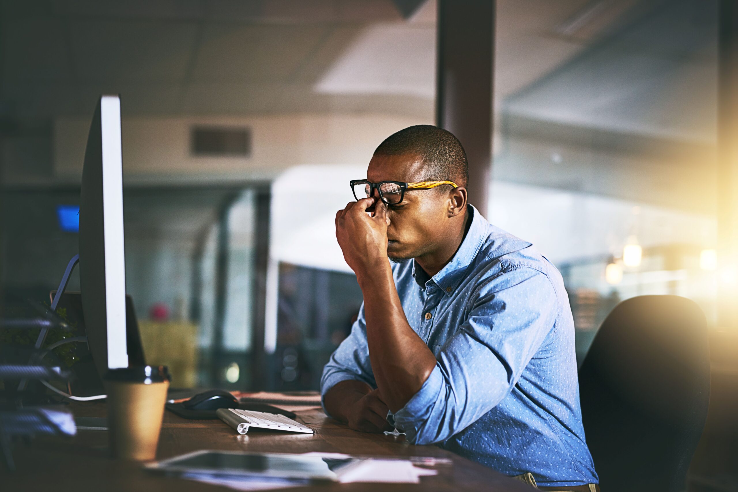 Stressed-out man sitting at desk pinching the bridge of his nose