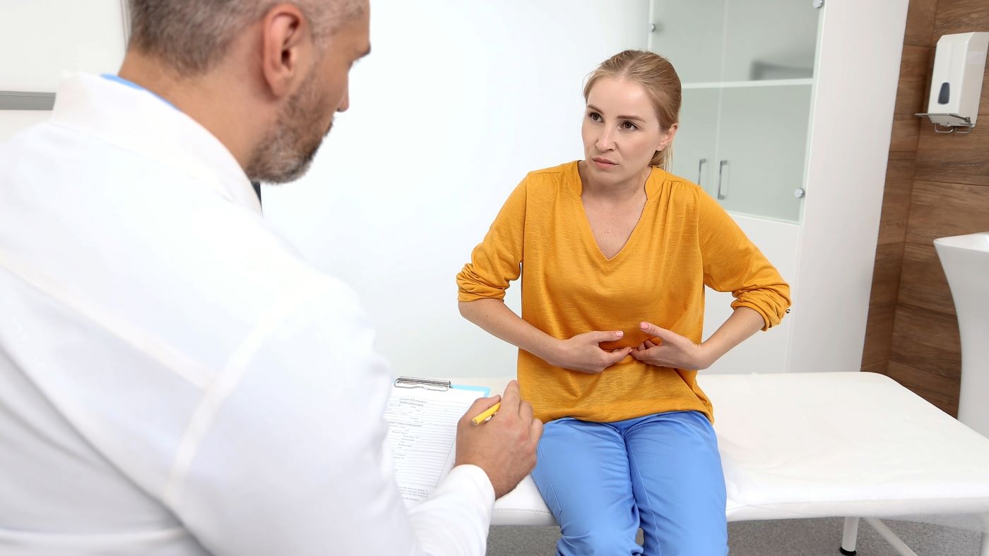 woman wearing orange shirt pressing on abdomen talking to doctor
